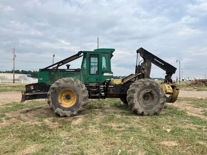 Green forestry tractor with large tires parked on grassy rural terrain
